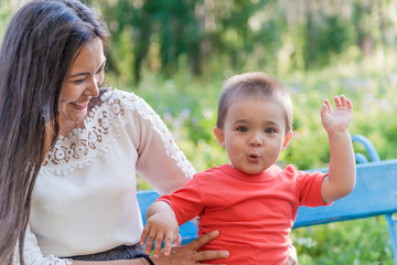  A happy young mother plays and has fun with her little son in the sun on a warm spring or summer day. The concept of a happy family, motherhood. Mother and child walk