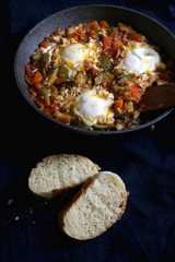 Shakshuka in a pan, with seasonal vegetables and eggs, and two slices of bread. Selective focus.