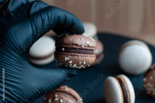 Fotografía Hand in black gloves holds a macaron with chocolate ganache and sesame seeds