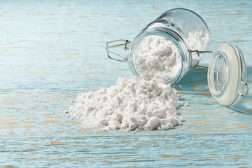 Cornstarch sprinkled from a glass jar on a  blue wooden table.