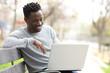 © PheelingsMedia - Happy black man using a laptop in a park