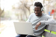 © PheelingsMedia - Happy black man watching media on laptop with headphones