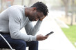 © PheelingsMedia - Sad black man complaining checking mobile phone