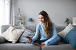 © BestForYou - Smiling young woman at home using modern smartphone.