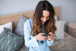 © BestForYou - Smiling young woman at home using modern smartphone.