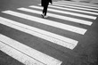 An abstract, wide view of a pedestrian crosswalk with white stripes and the legs of a woman walking away.