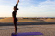 © Josu Ozkaritz - Slim woman practices sun salutation yoga pose at sunrise by Maspalomas sand dunes in Gran Canaria, Spain. Female yogi standing alone on purple mat with arms up at dawn. Outdoors workout concept
