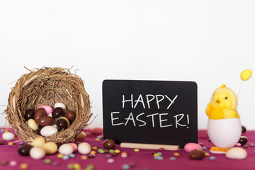 Canvas Print - Bird nest full of easter almond eggs, decorative chick and blackboard with the text Happy Easter