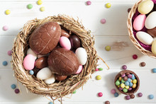 Top View Of Bird Nest With Chocolate Eggs And Easter Almonds And Sweets On White Wooden Table