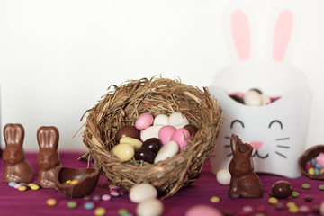 Wall Mural - Easter almond eggs on nest, chocolate bunny and treat box with sweets against white background