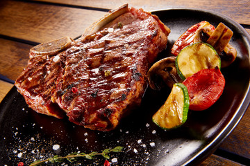 Grilled beef steak with rosemary, salt and pepper on black stone plate. Grilled striploin sliced steak. Juicy thick grilled beef steak seasoned with rosemary fresh of the summer BBQ.