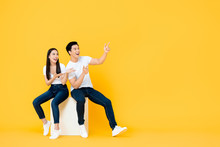 Happy Surprised Attractive Young Asian Couple Pointing And Looking At Blank Space Beside In Yellow Isolated Stuidio Background