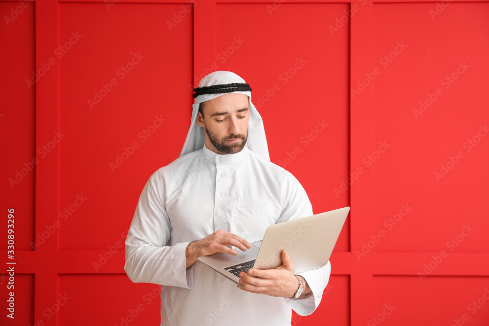 Handsome Arab man with laptop on color background