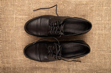 A pair of black leather boots with lacing on a background of coarse fabric. Close up.