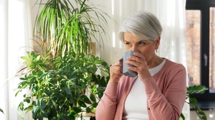 Sticker - age, drink and people concept - happy smiling senior woman with cup of tea or coffee at home