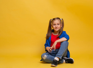 nice lovely cute attractive cheerful young girl sitting on the floor in jeans red t-shirt and blu jacket looking at you on yellow background