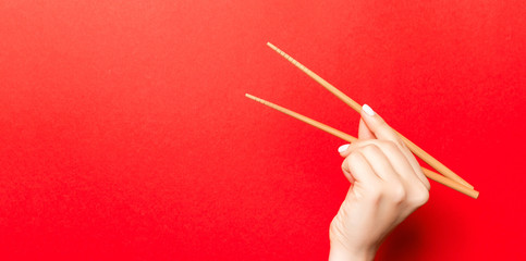 Wall Mural - Creative image of wooden chopsticks in female hand on red background. Japanese and chinese food with copy space