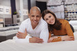 © Ihor - Happy young couple smiling to the camera, lying on orthopedic mattress at furniture store. Buying new bed concept