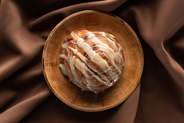 Wall Mural - top view of fresh homemade cinnamon roll on plate on silk brown cloth