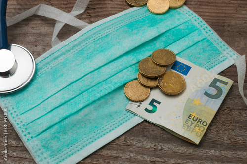 Cuadros en Lienzo Medical face mask on a wooden table with euro coins and a five euro banknote on top of it