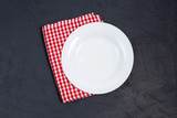Fototapeta  - Empty white plate and red napkin on black table.