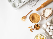 Set Of Various Baking Ingredients - Flour, Eggs, Sugar, Butter, Nuts, Kitchen Utensils And Cupcake Baking Dish On White Background. Top View.