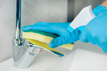 Woman With Blue Nitrile Gloves Disinfects The Sink Mixer After Washing Her Hands To Avoid The Proliferation Of Viruses And Bacteria