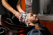 © AJ_stock_photos - a young dark-haired guy of Indian or Asian appearance in a Barber shop on a black chair. the Barber washes his head with shampoo.