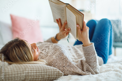 Cuadros en Lienzo Young woman lies on her back in bed reading a book