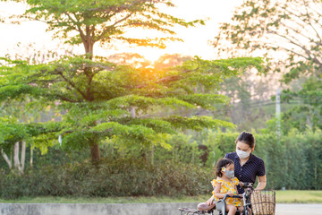 Wall Mural - Mother and daughter wearing medical face mask prevent flu, pollution and covid 19 riding bicycle at park.