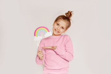 A happy girl holds a rainbow in the clouds made of felt. Spring portrait on a light background with space for text. Concept of the Easter holiday