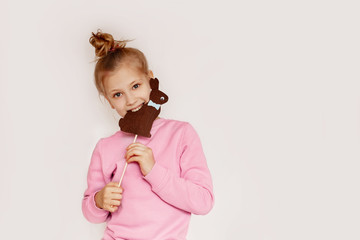 A cheerful girl holds in her hands and bites a brown rabbit made of felt. Easter portrait of a beautiful girl in pink on a light background and a place for text. Concept of the Easter holiday