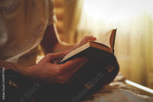 Fotografía Young man reading book on bed at home, closeup