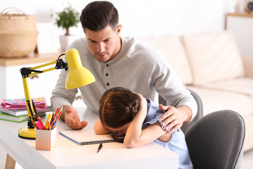 Wall Mural - Father scolding his daughter while helping with homework at table indoors