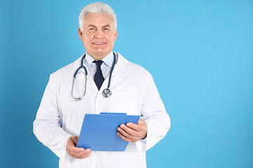 Canvas Print - Portrait of senior doctor with clipboard against blue background, space for text