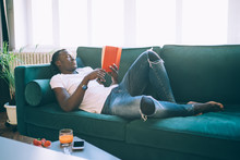 Thoughtful Black Man Reading Book With Comfort  On Sofa