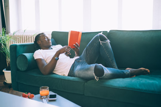 Thoughtful black man reading book with comfort  on sofa