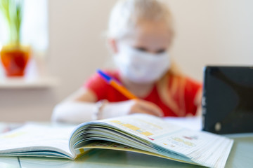 Wall Mural - Distance learning online education. Blurred sickness schoolgirl in medical mask studying at home with digital tablet in hand and doing school homework. Training books and notebooks on table