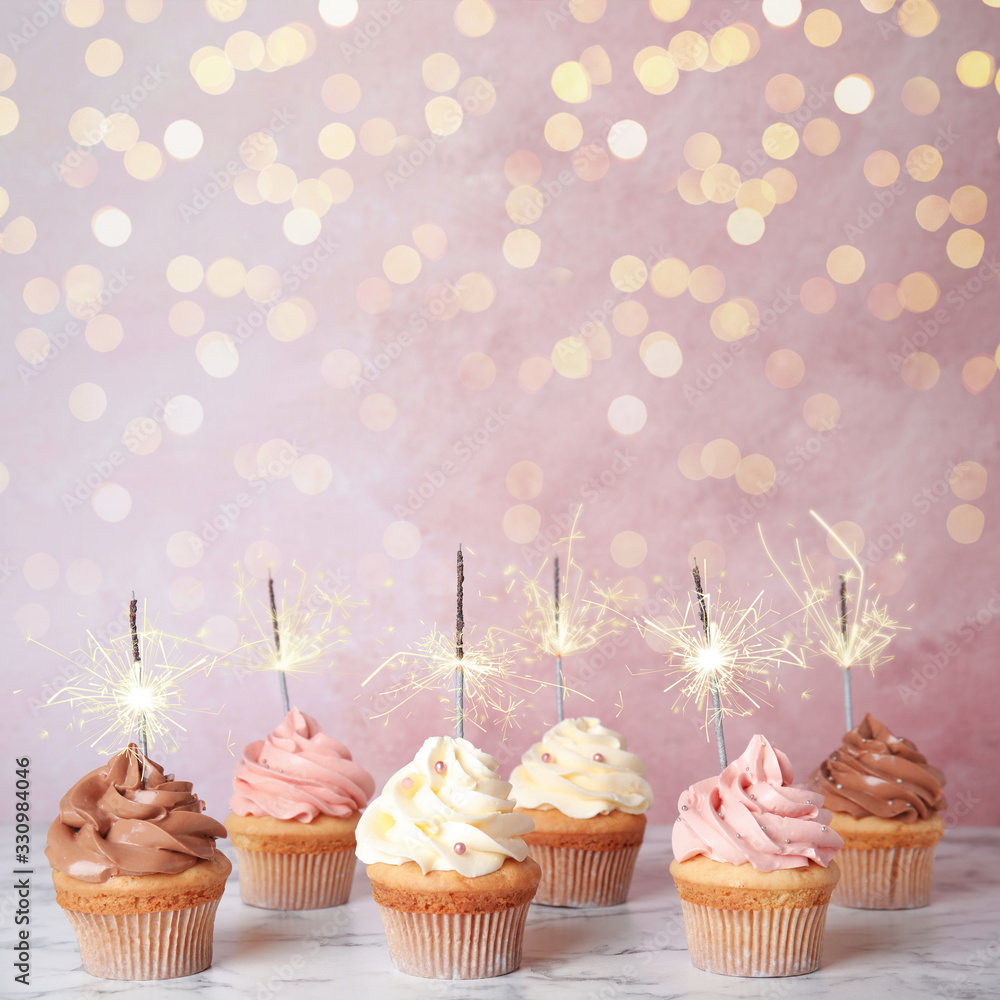 Birthday cupcakes with sparklers on table against light pink background - obrazy, fototapety, plakaty 