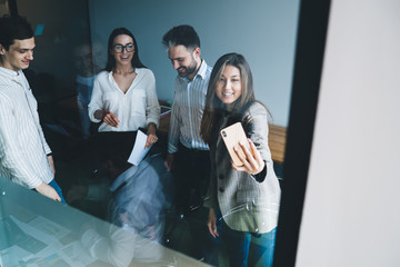 Wall Mural - Friendly female employee taking selfie with coworkers