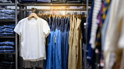 Wall Mural - White T-shirt hanging on rack in clothes shop with shirt and dress beside. Summer collection fashion product samples in clothing store for selling. Textile industry and business concept