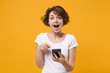 © ViDi Studio - Excited young brunette woman girl in white t-shirt posing isolated on yellow orange background studio portrait. People lifestyle concept. Mock up copy space. Pointing index finger on mobile phone.
