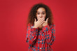 © ViDi Studio - Shocked young african american girl in pajamas homewear posing while resting at home isolated on red wall background. Relax good mood lifestyle concept. Mock up copy space. Covering mouth with hands.