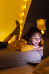 Wall Mural - little 11 year old girl using laptop under her home-made tent inside the living room.