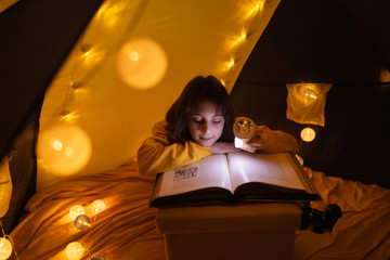 Wall Mural - young female child reading encyclopedia in a home made livingroom tent with light balls.