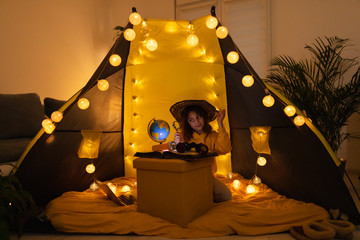 Wall Mural - young female child using magnifying glass to explore earth globe in a home made livingroom tent with