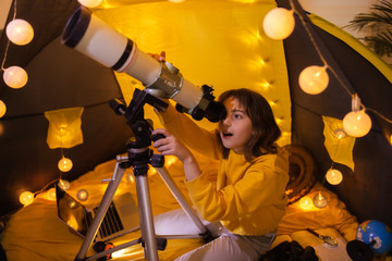Wall Mural - small girl using telescope at home living room in a tent.