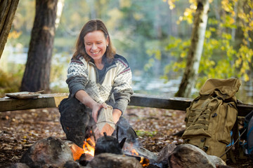 Wall Mural - Man and woman making coffee in big kettle on campfire in forest on shore of lake, making a fire, grilling. Happy couple exploring Finland. Scandinavian landscape. 