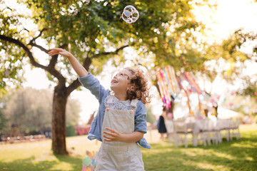 Portrait of small girl playing with bubbles outdoors on garden party in summer.