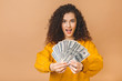 © denis_vermenko - Portrait of a cheerful young curly woman holding money banknotes and celebrating isolated over beige background.